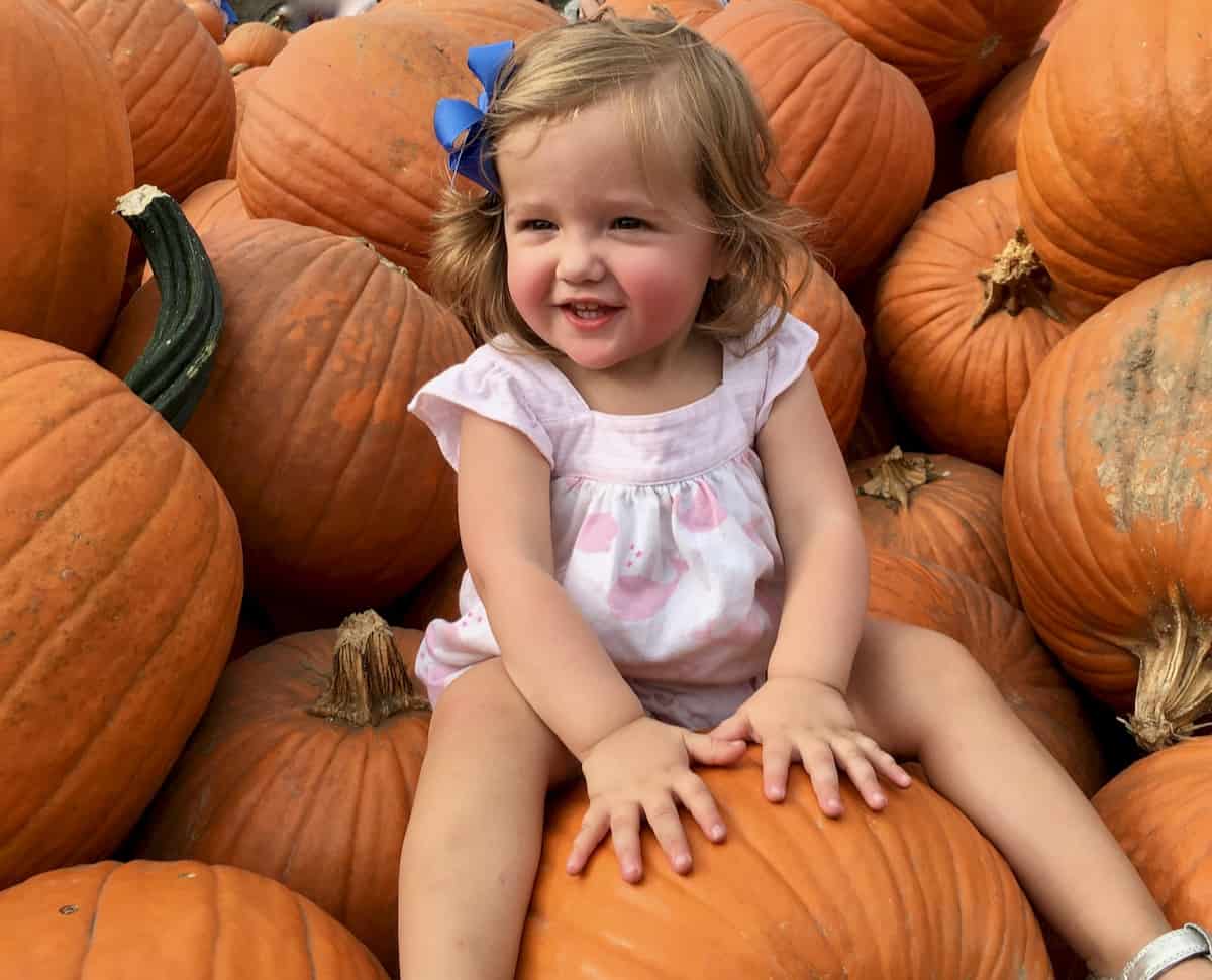 My grand daughter sitting in pile of pumpkins.