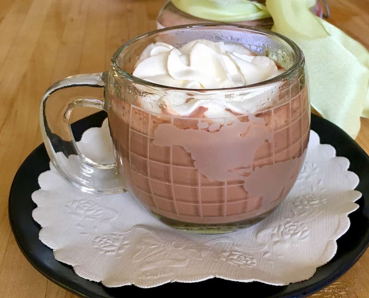 Cup of prepared decadent hot chocolate on a black plate lined with a doily.