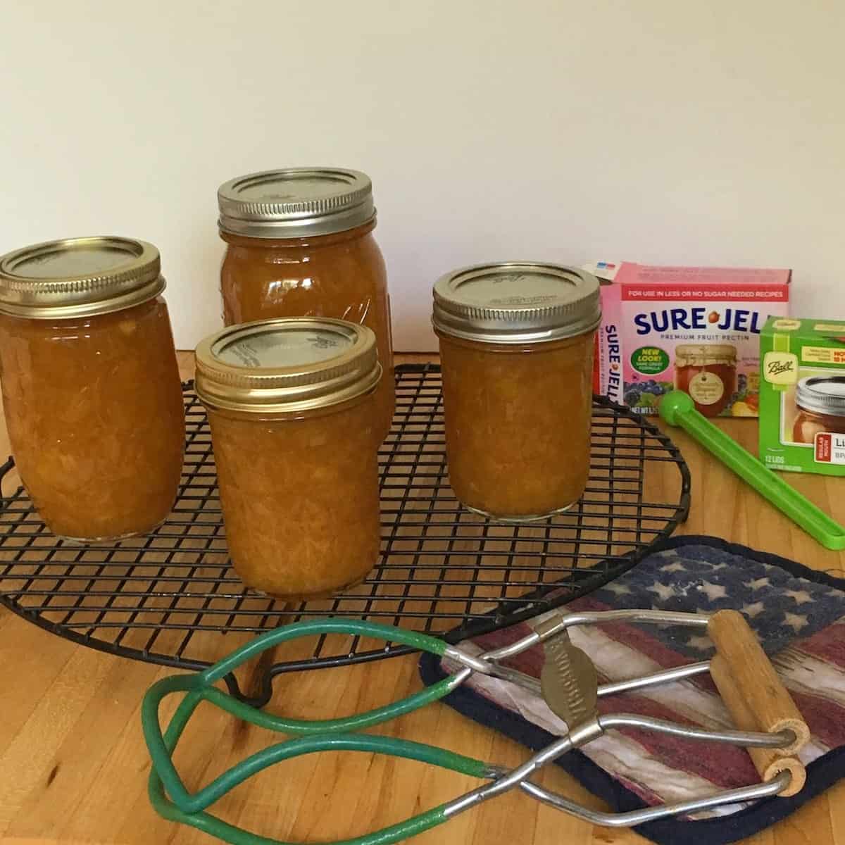 Jars of the best peach jam with canning supplies.