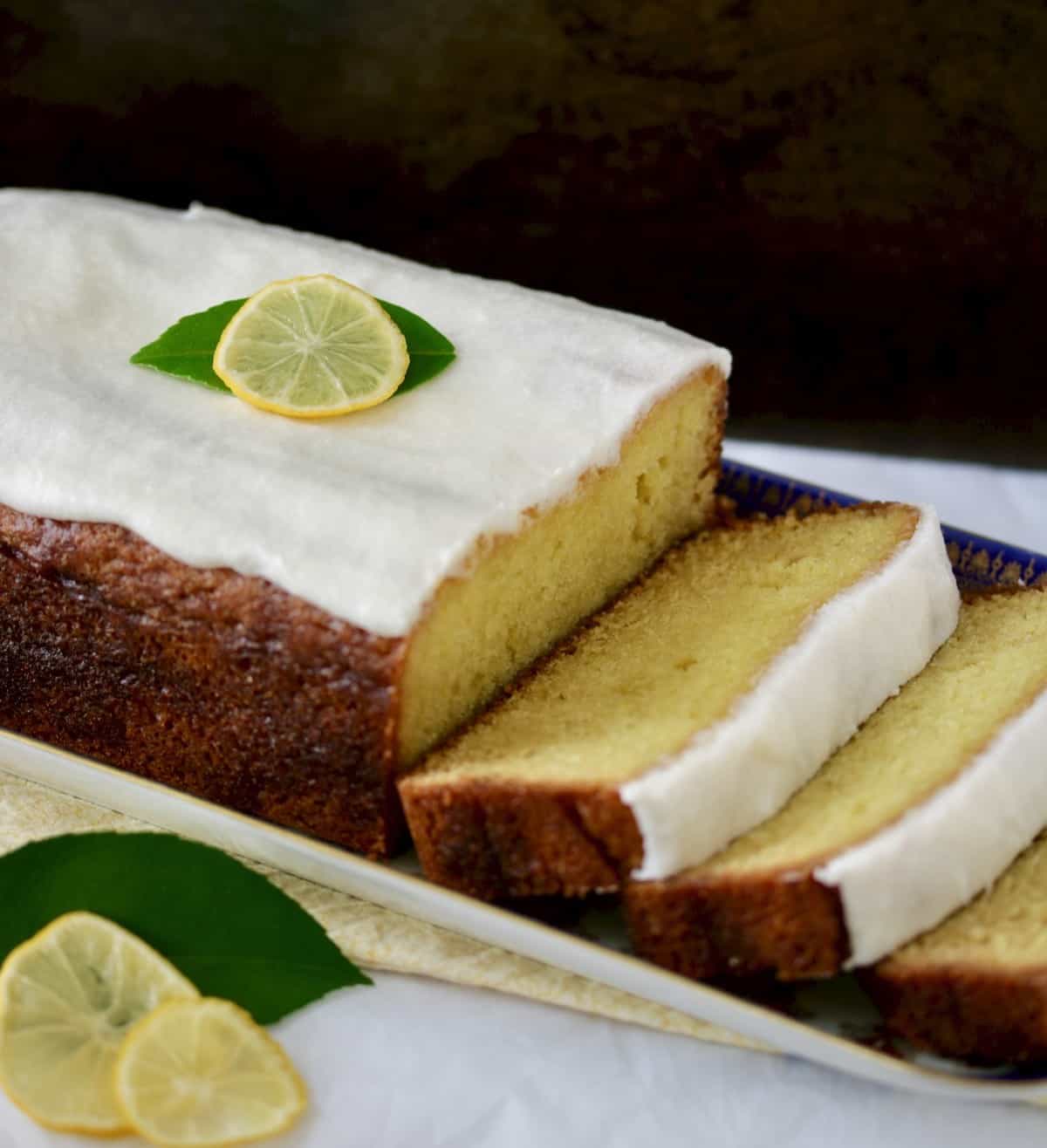 Sliced lemon loaf with white icing and lemon slice garnish.