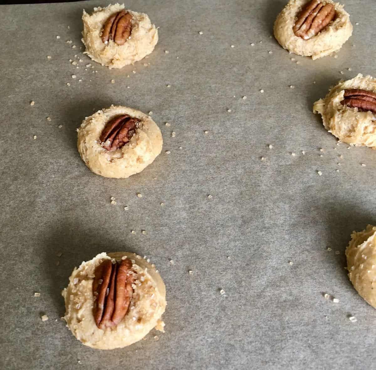 Unbaked cookies topped with pecan and sprinkled with sugar.