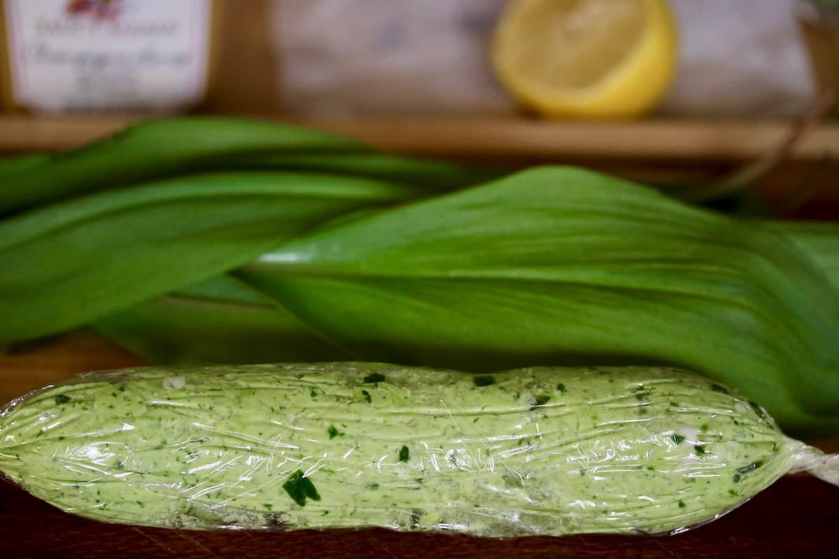 Foraged ramp butter wrapped in plastic with ingredients in background.