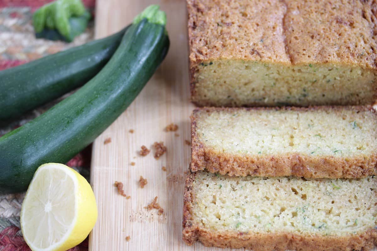 Sliced zucchini bread with fresh zucchini and lemon.