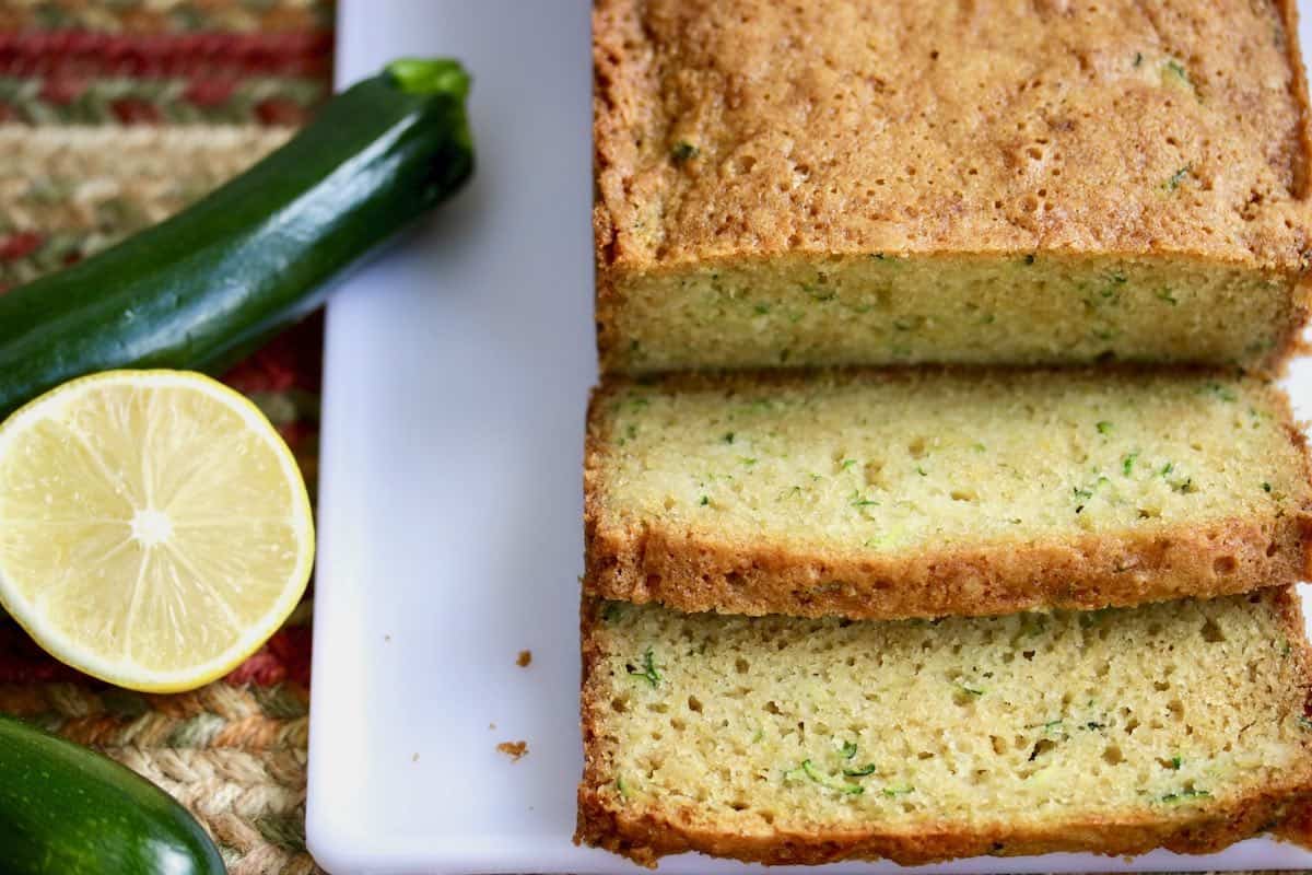 Sliced zucchini bread with fresh zucchini and lemon.